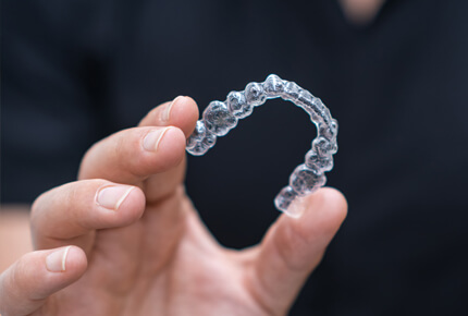 Person holding clear orthodontic aligner retainer against dark background.