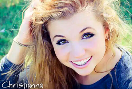 Young woman smiling at camera outdoors with blonde hair and blue eyes, casual portrait.