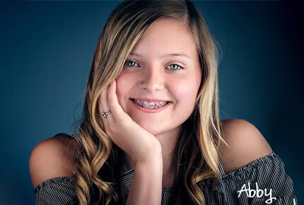 Young woman smiling at camera, hand to face, blue background studio portrait