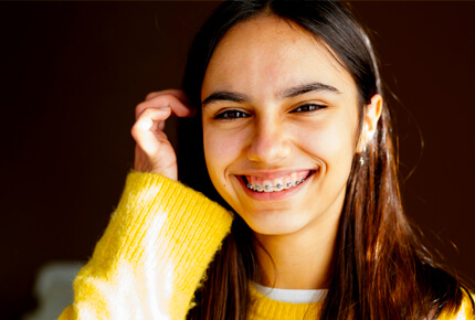 Young girl smiling at camera wearing yellow sweater against dark background.