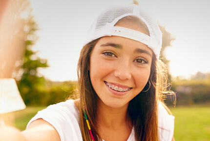 Smiling young woman wearing white cap outdoors in sunny park setting.