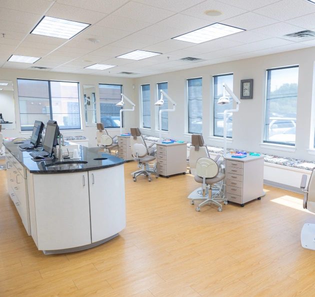 Modern orthodontic office treatment room with dental chairs, equipment, and bright natural lighting.