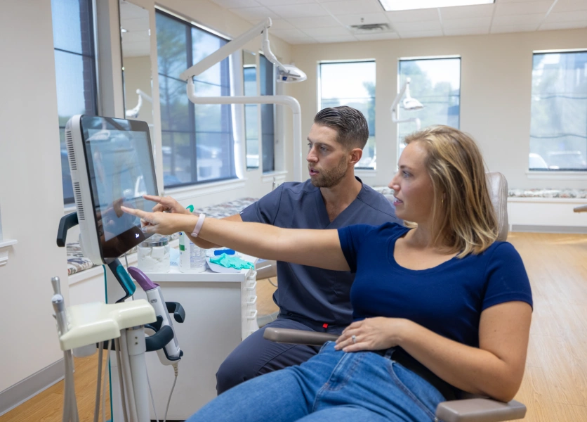 Orthodontist and patient reviewing digital scan results on computer monitor in clinical office.