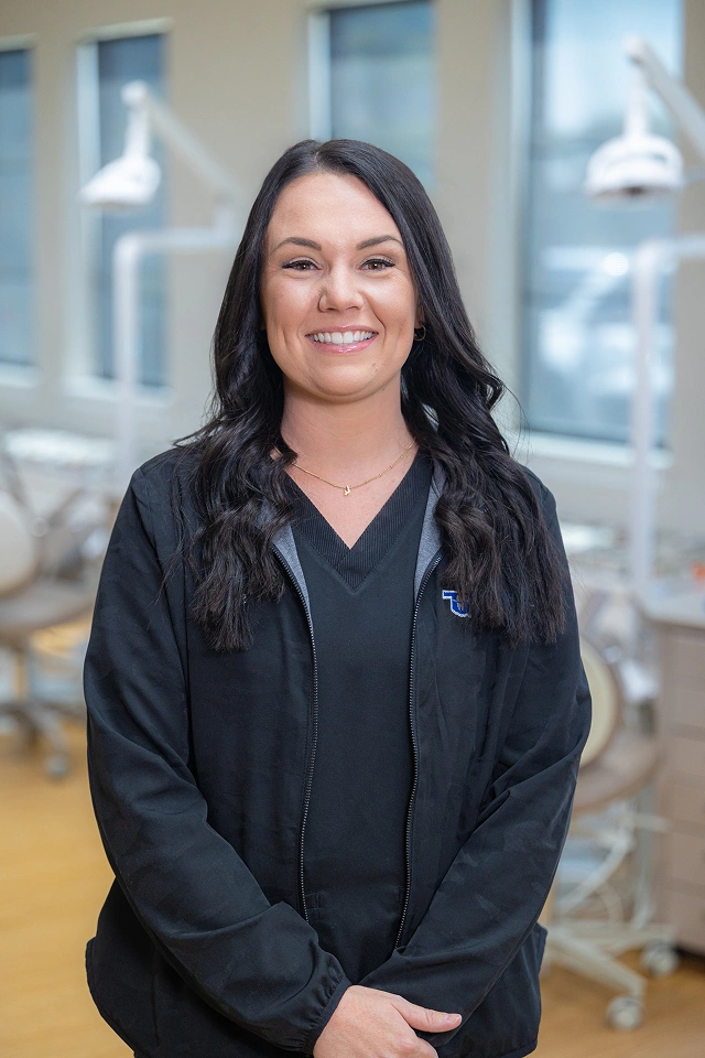 Professional woman in black hoodie smiling at orthodontics office with modern interior background.