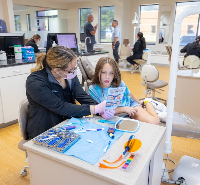 Orthodontist assists young patient with educational materials at dental office reception desk.
