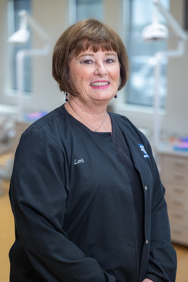 Professional orthodontist wearing black scrubs smiling in modern dental office setting.