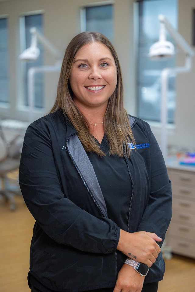 Professional woman in dark blazer smiling in modern orthodontic office setting.