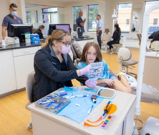 Orthodontist demonstrating dental model to young patient in bright clinical treatment room.